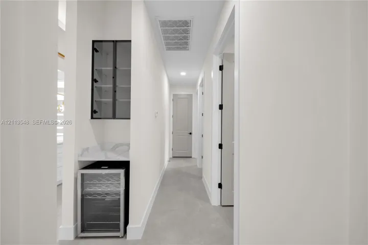 Built-in refreshment station featuring stone-composite countertop, glass-front cabinetry, and under-counter beverage cooler, complemented by neutral tile flooring and solid-core paneled doors