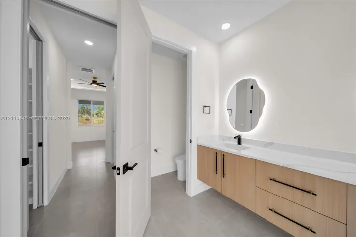 Floating wood-finish vanity with light-toned cabinetry, dual-drawer storage, integrated sink, and quartz countertop, complemented by an illuminated organic-shaped mirror and matte black fixtures
