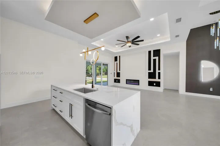 Kitchen island with stone-finish countertop, undermount stainless steel sink, and integrated dishwasher, complemented by a tray ceiling with recessed lighting and a built-in linear fireplace
