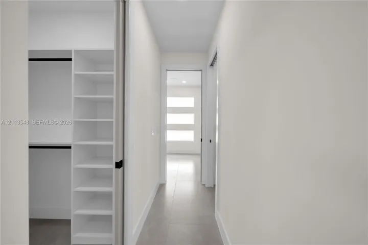 Walk-in closet featuring white built-in shelving, matte black hardware, and tile flooring