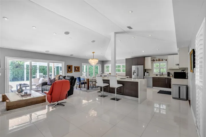 Open-concept interior featuring large-format tile flooring, vaulted ceilings with recessed lighting, kitchen island with quartz-style countertop, and dual sliding glass doors