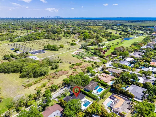 Aerial perspective featuring a residential lot with a rectangular swimming pool, concrete hardscaping, and mature perimeter landscaping