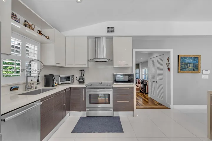 Kitchen featuring two-tone flat-panel cabinetry, quartz countertops, stainless steel appliances, a professional-style pull-down faucet, and polished tile flooring