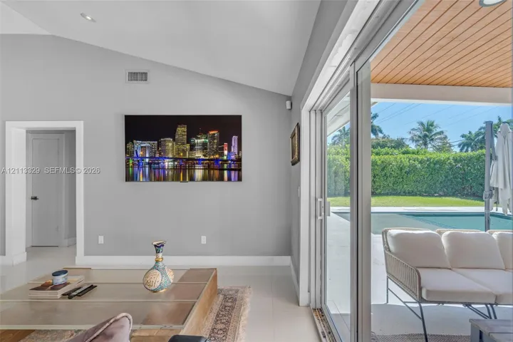 Vaulted ceilings, large-format tile flooring, and floor-to-ceiling sliding glass doors opening to a covered patio with wood-paneled ceiling, manicured landscaping, and a pool