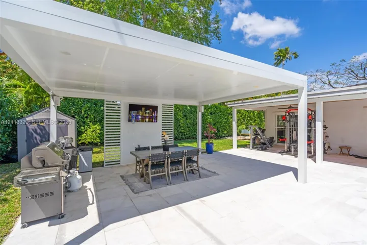 Covered outdoor patio featuring a flat-roof structure with recessed lighting, light-toned stone tile flooring, and vertical slatted privacy screening