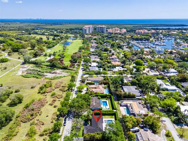 Aerial perspective showcasing a residential property featuring a private swimming pool, mature perimeter landscaping, and proximity to regional coastal waterways and golf course grounds