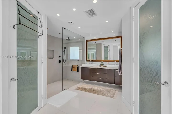 Floating dark-wood cabinetry with dual rectangular vessel sinks, walk-in glass-enclosed shower featuring matte black fixtures, and large framed wall mirror
