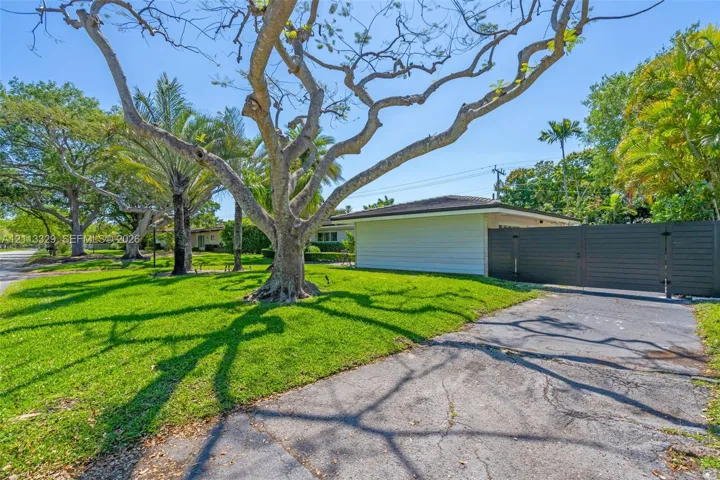 Expansive grass lawn featuring mature trees, horizontal exterior siding, and a dark-toned privacy fence