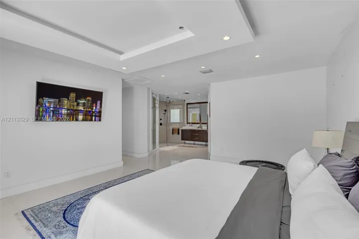 Tray ceiling with recessed lighting, large-format tile flooring, and en-suite bathroom featuring a dark wood vanity