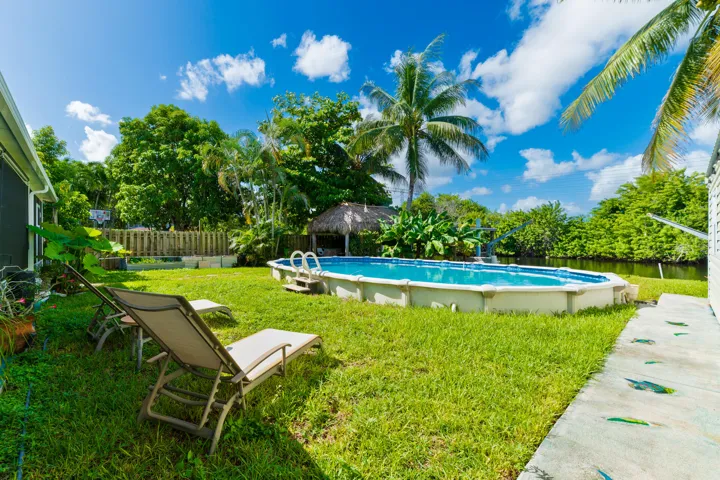 Backyard featuring an above-ground pool, grass lawn, thatch-roofed cabana, and water frontage