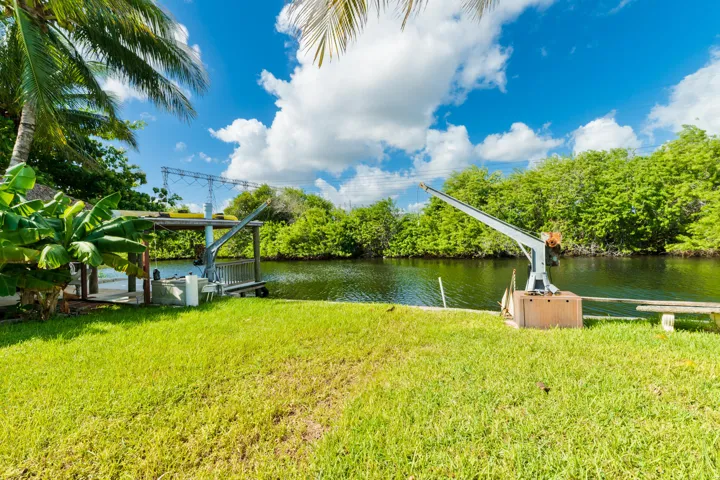 Waterfront grounds featuring a grass lawn, boat davits, and a covered dock structure