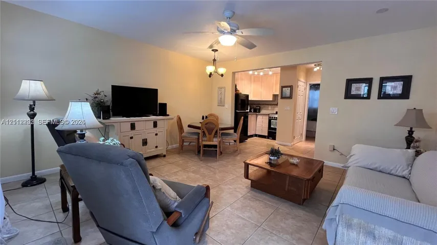 Open-concept interior featuring large-format tile flooring, a ceiling fan with integrated lighting, a multi-arm chandelier, and kitchen cabinetry with matching appliances