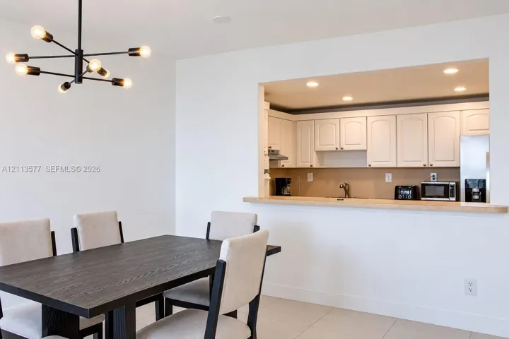 Modern black metal sputnik chandelier, white cabinetry, solid-surface breakfast bar, recessed lighting, and tile flooring