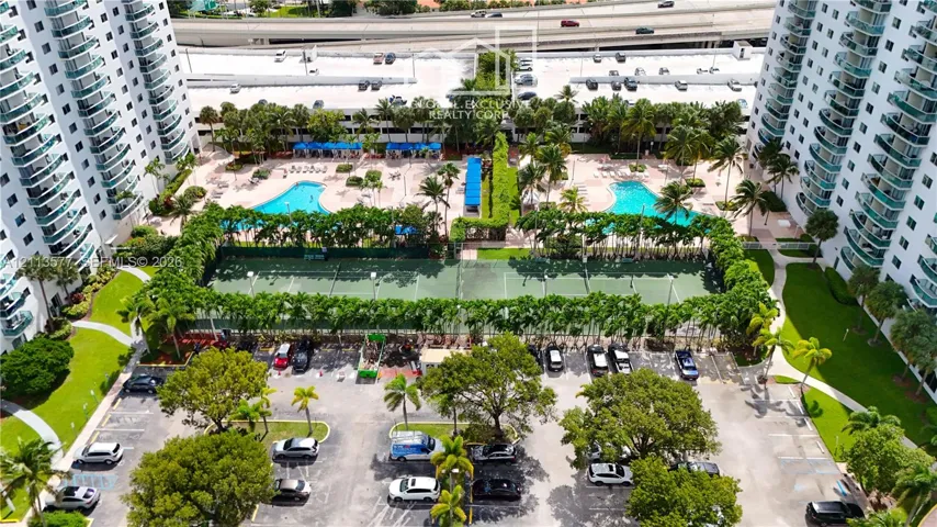 High-rise community featuring dual outdoor swimming pools, multi-court tennis facilities, paved parking, and landscaped grounds