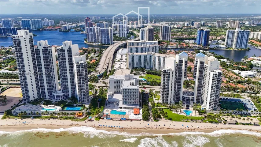 Aerial perspective of waterfront high-rise residential towers featuring direct beach access, outdoor swimming pools, and tennis courts