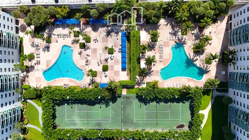 Recreational area featuring two outdoor swimming pools, two hard-court tennis courts, paved decking, and mature landscaping