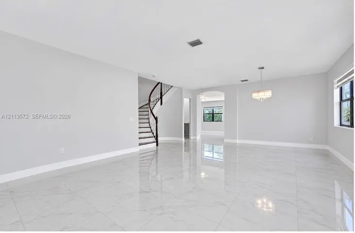 Open-concept interior featuring large-format polished stone-finish flooring, a curved staircase with a dark wood handrail, an arched entryway, and a tiered drum chandelier
