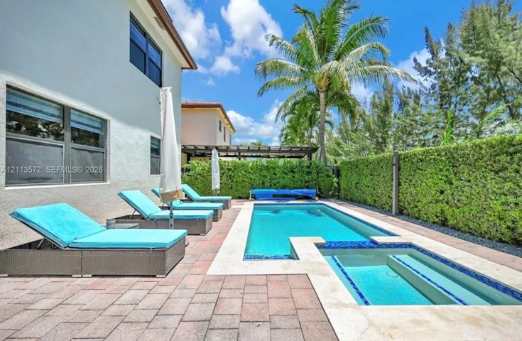 Rear patio featuring a swimming pool with integrated spa, paver hardscaping, and privacy hedges