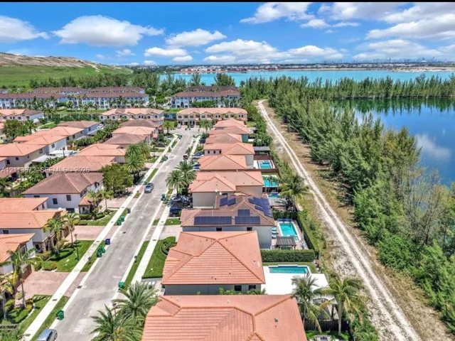 Aerial perspective of residential neighborhood featuring tile-roofed structures, solar panel arrays, private swimming pools, and waterfront placement