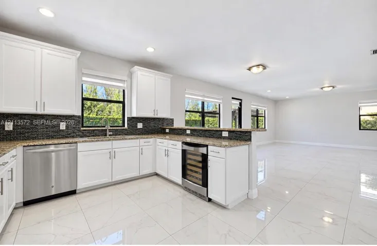 Kitchen featuring white shaker-style cabinetry, stone countertops, a dark-toned tile backsplash, stainless steel appliances, and polished tile flooring