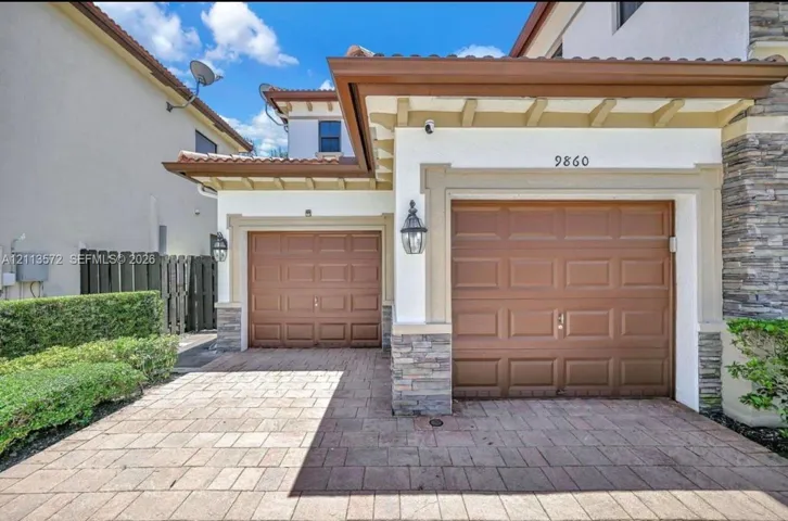 Stucco exterior with stone veneer accents, dual-car garage with paneled doors, and paved driveway