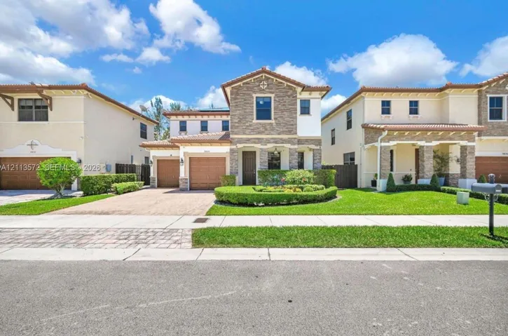 Two-story residence featuring a stone-veneer façade, clay tile roof, dual-car garage, and a manicured front lawn