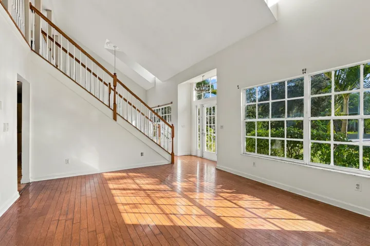 Vaulted ceilings, wood-finish flooring, staircase with wood railings, multiple pane windows, and a glass-paneled entry door
