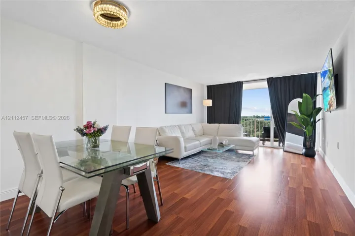 Open-concept living space featuring wood-finish flooring, a contemporary circular crystal ceiling light fixture, and floor-to-ceiling glass sliding doors leading to a private balcony