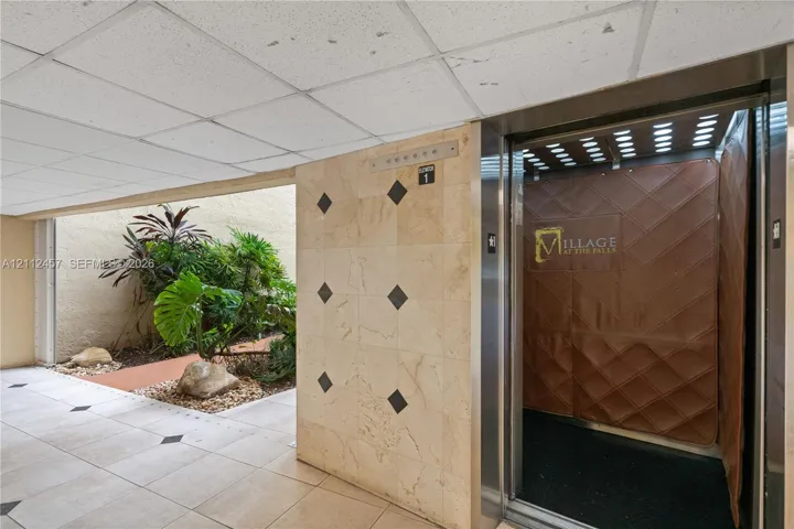 Elevator lobby featuring square tile flooring with black accent insets, polished light-toned stone wall cladding, and an integrated plant bed with stone ground cover