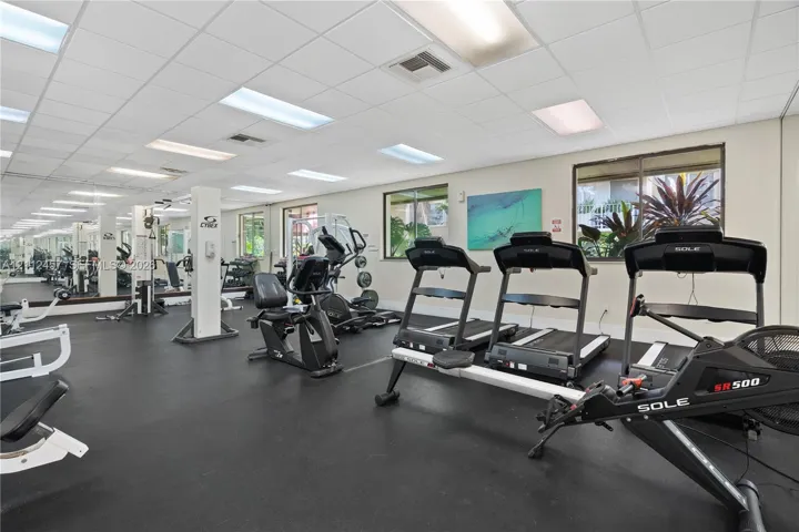 Fitness space featuring impact-resistant rubber flooring, full-length wall mirrors, drop-ceiling lighting, and multiple windows