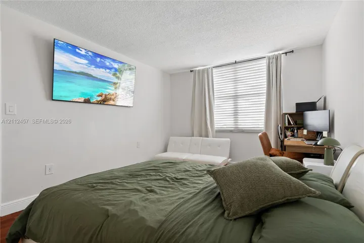 Neutral-toned walls, wood-finish flooring, and a large window featuring horizontal blinds and curtain hardware