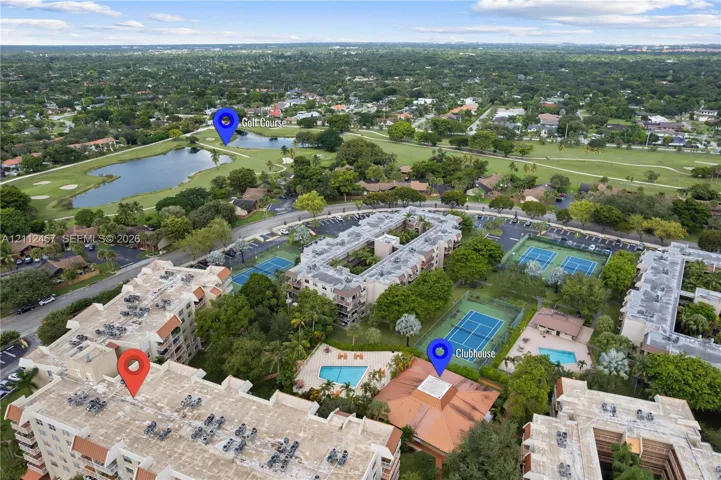 Aerial perspective of residential complex featuring a community clubhouse, outdoor swimming pools, and tennis courts, positioned near a golf course and water features