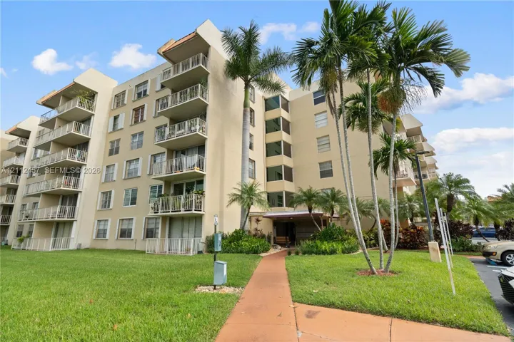 Multi-story residential building featuring private balconies, stucco exterior, concrete walkway, and mature palm trees