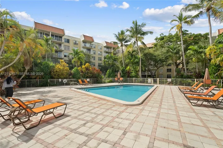 Swimming pool featuring a concrete paver deck, metal perimeter fencing, and mature palm trees