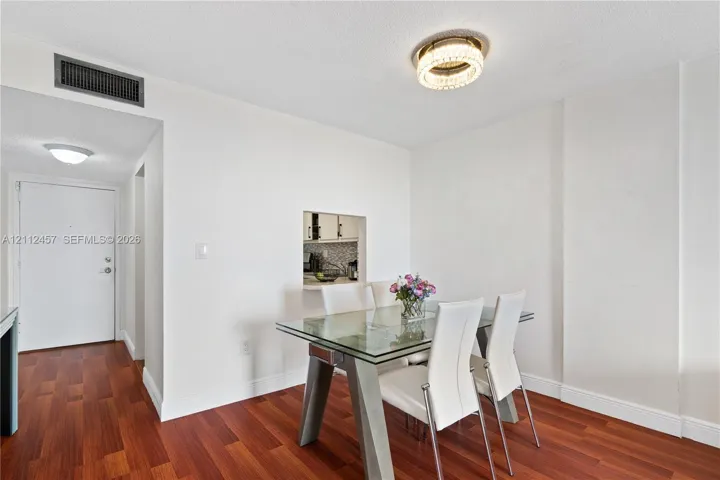 Dining area featuring wood-finish flooring, a wall cut-out pass-through to the kitchen, and a circular crystal-style flush-mount ceiling fixture