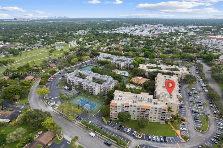 Aerial perspective of a multi-story residential complex featuring multiple tennis courts, designated surface parking, manicured landscaping, and a central swimming pool