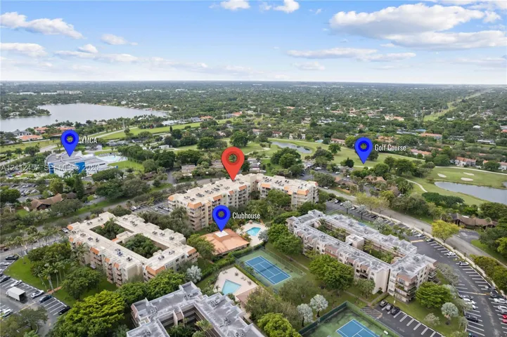 Aerial perspective of multi-story residential buildings featuring a community clubhouse, outdoor swimming pool, and tennis courts