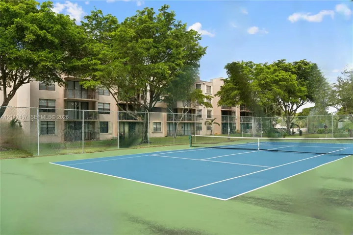 Tennis court featuring a hard surface, perimeter fencing, and mature surrounding trees