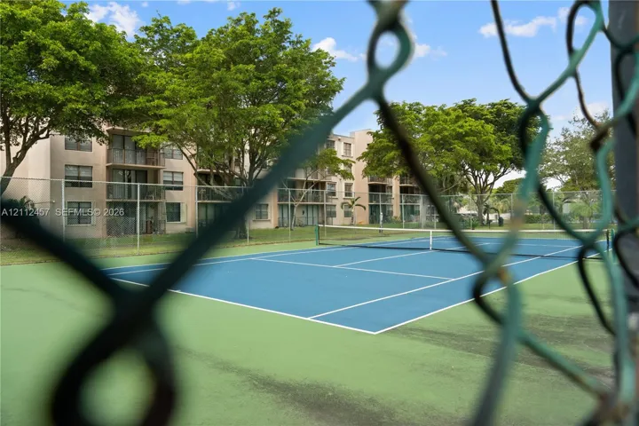 Tennis court with hard surface, chain-link perimeter fencing, and mature trees