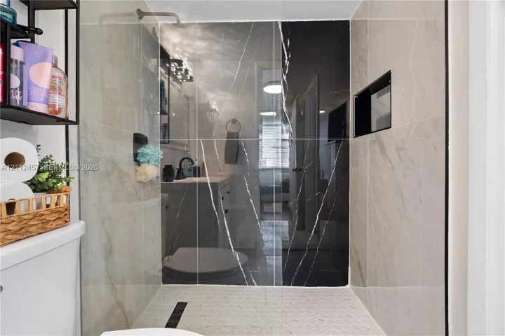 Walk-in shower featuring large-format light and dark veined tile, integrated wall niche, and hexagonal floor tile
