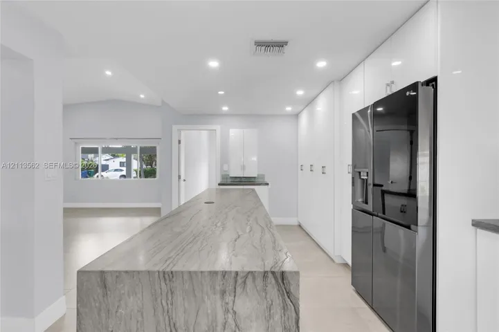 Kitchen featuring a large central island with waterfall-edge countertop, floor-to-ceiling high-gloss white cabinetry, large-format tile flooring, and integrated stainless steel refrigerator