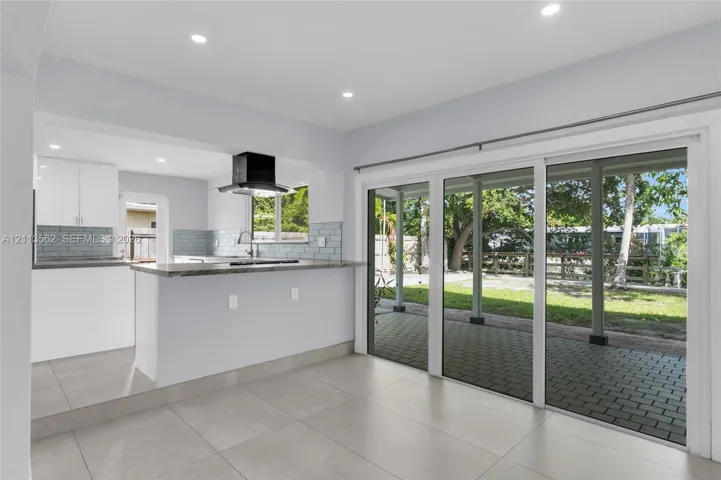 Kitchen featuring white cabinetry, a stone-surface breakfast bar, a modern range hood, and tile backsplash, with large sliding glass doors leading to a paved patio