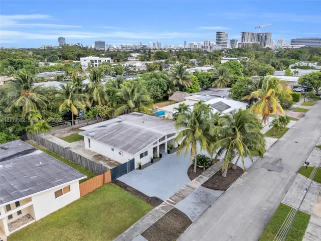 Single-story residence featuring a flat roofline, paved driveway, integrated solar panels, and mature palm landscaping
