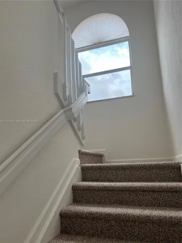 Staircase featuring wall-to-wall carpeting, white painted wooden handrails, and a fixed arched window with integrated screen