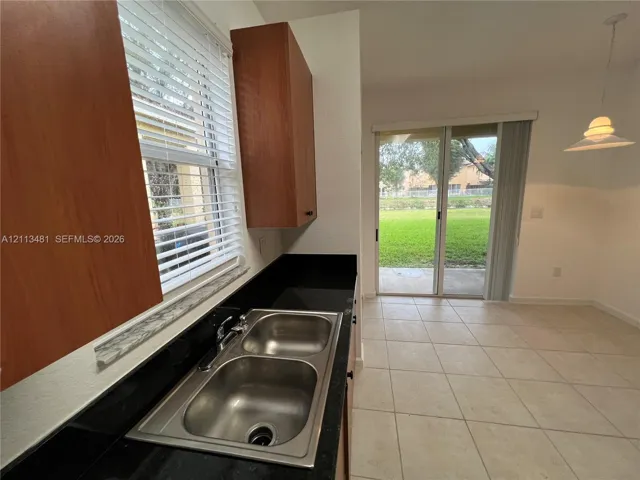 Kitchen featuring dark stone countertops, dual-basin stainless steel sink, wood-finish cabinetry, ceramic tile flooring, and sliding glass door access to the exterior