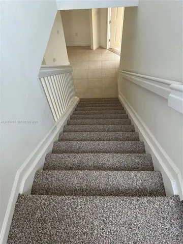 Staircase featuring neutral-tone carpeting, white painted handrails, and a white balustrade