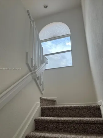 Staircase featuring carpeted treads, white wooden handrails, and an arched window with integrated top-light