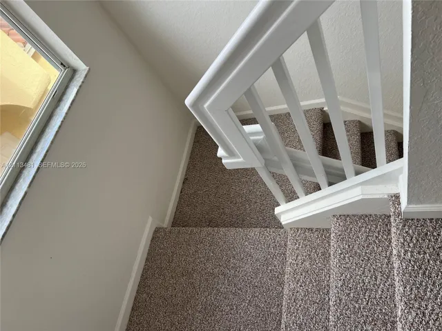 Staircase featuring wall-to-wall carpeting, white painted wooden balusters, and a rectangular window