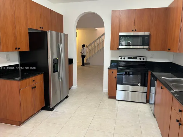 Kitchen featuring wood-finish cabinetry, stone countertops, stainless steel appliances, and a prominent arched entryway