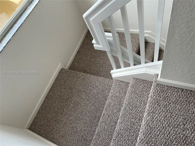 Staircase featuring wall-to-wall carpeting, white wooden balusters, and a matching handrail